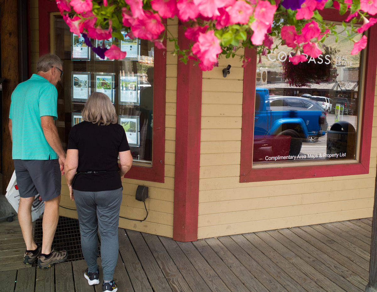 A couple examines a real estate window in Jackson on July 15, 2024, a town where most workers can't afford to buy a home. (Angus M. Thuermer Jr./WyoFile)