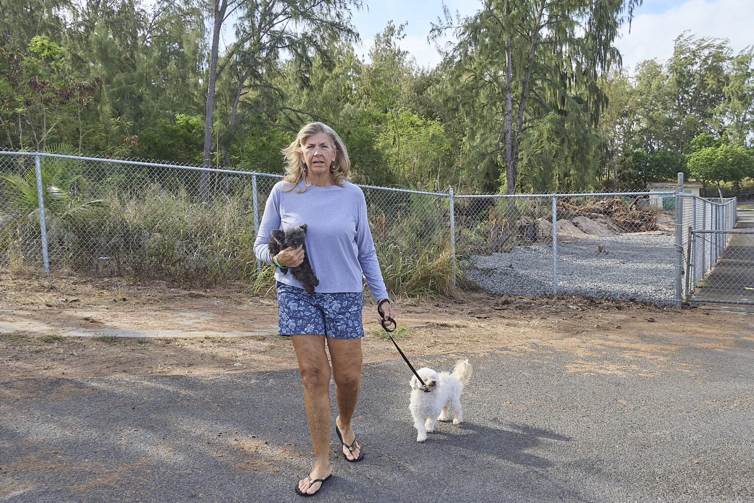 Evelyn Lane was walking her dogs in August 2024 when she turned and saw a fire in the ironwood grove, seen behind her here, up the road near her home at Kahuku Hauoli Hale. (David Croxford/Civil Beat/2025)