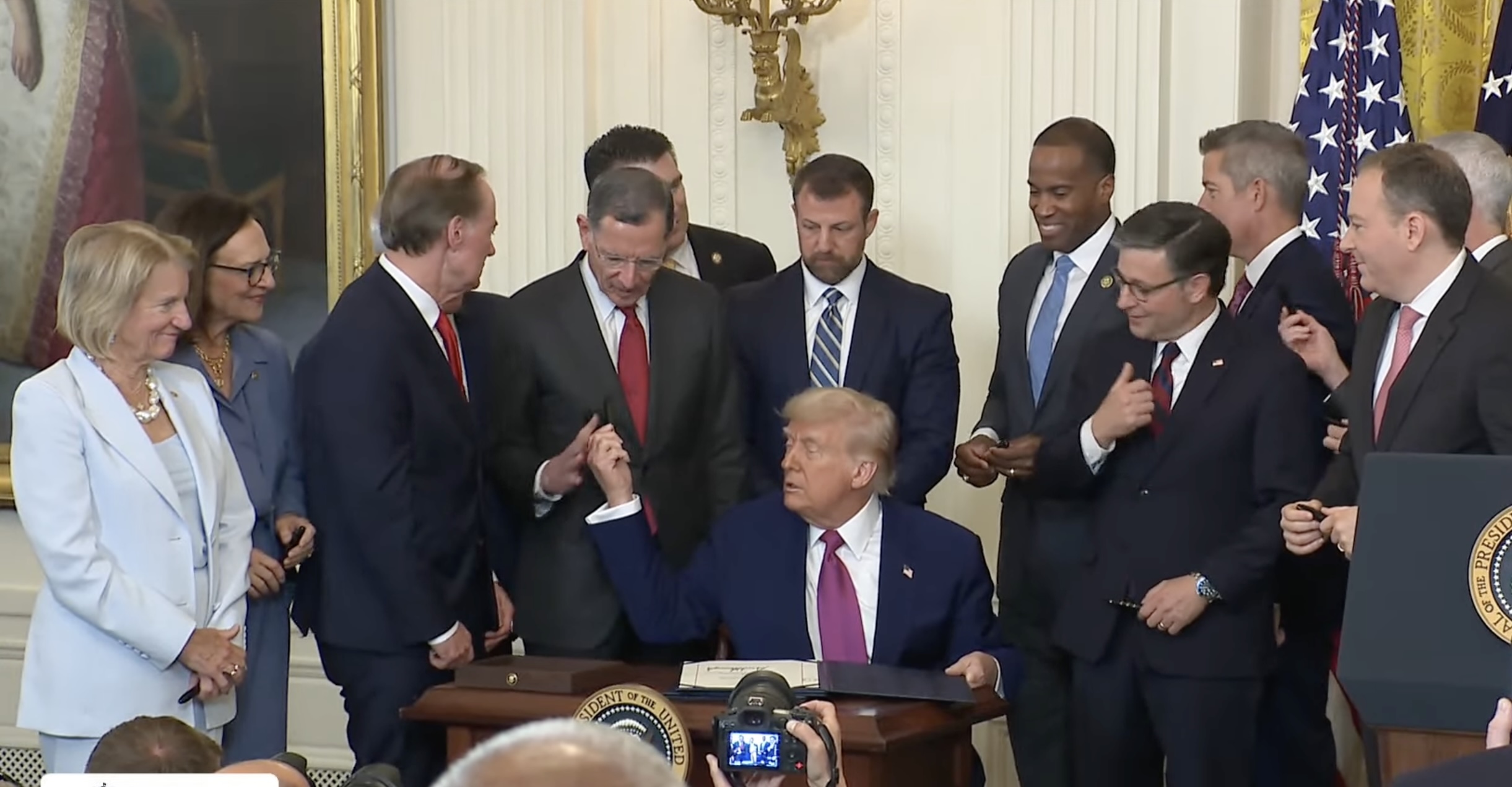 President Donald Trump signs a Congressional Review Act resolution Thursday, with congressional Republicans looking on. Left to right are Sen. Shelley Moore Capito of West Virginia, Sen. Deb Fischer of Nebraska, Rep. John Joyce of Pennsylvania, Sen. John Barrasso of Wyoming, Sen. Markwayne Mullin of Oklahoma, Rep. John James of Michigan, House Speaker Mike Johnson of Louisiana, Transportation Secretary Sean Duffy and EPA Administrator Lee Zeldin. (Screeenshot from White House webcast)