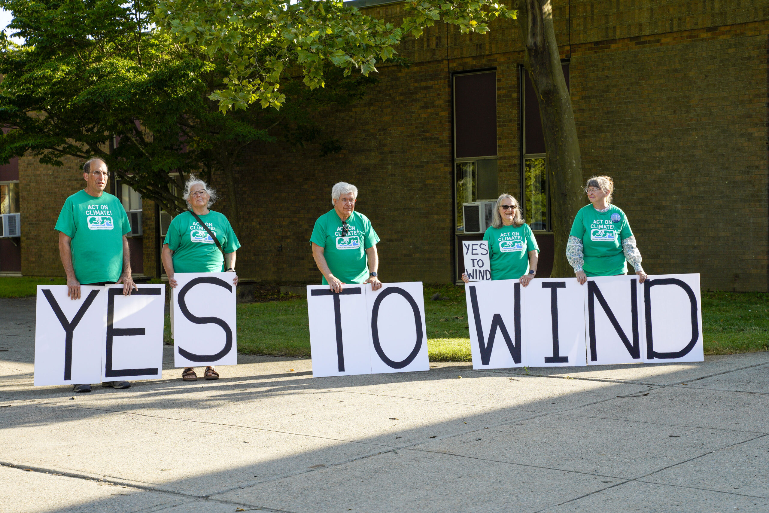 Members of Climate Action Rhode Island show their support for the South Coast Wind project outside Portsmouth Middle School on July 23, 2025. The Rhode Island Energy Facility Siting Board held a hearing on SouthCoast Wind’s cable burial plan that night. (Photo by Laura Paton/Rhode Island Current)