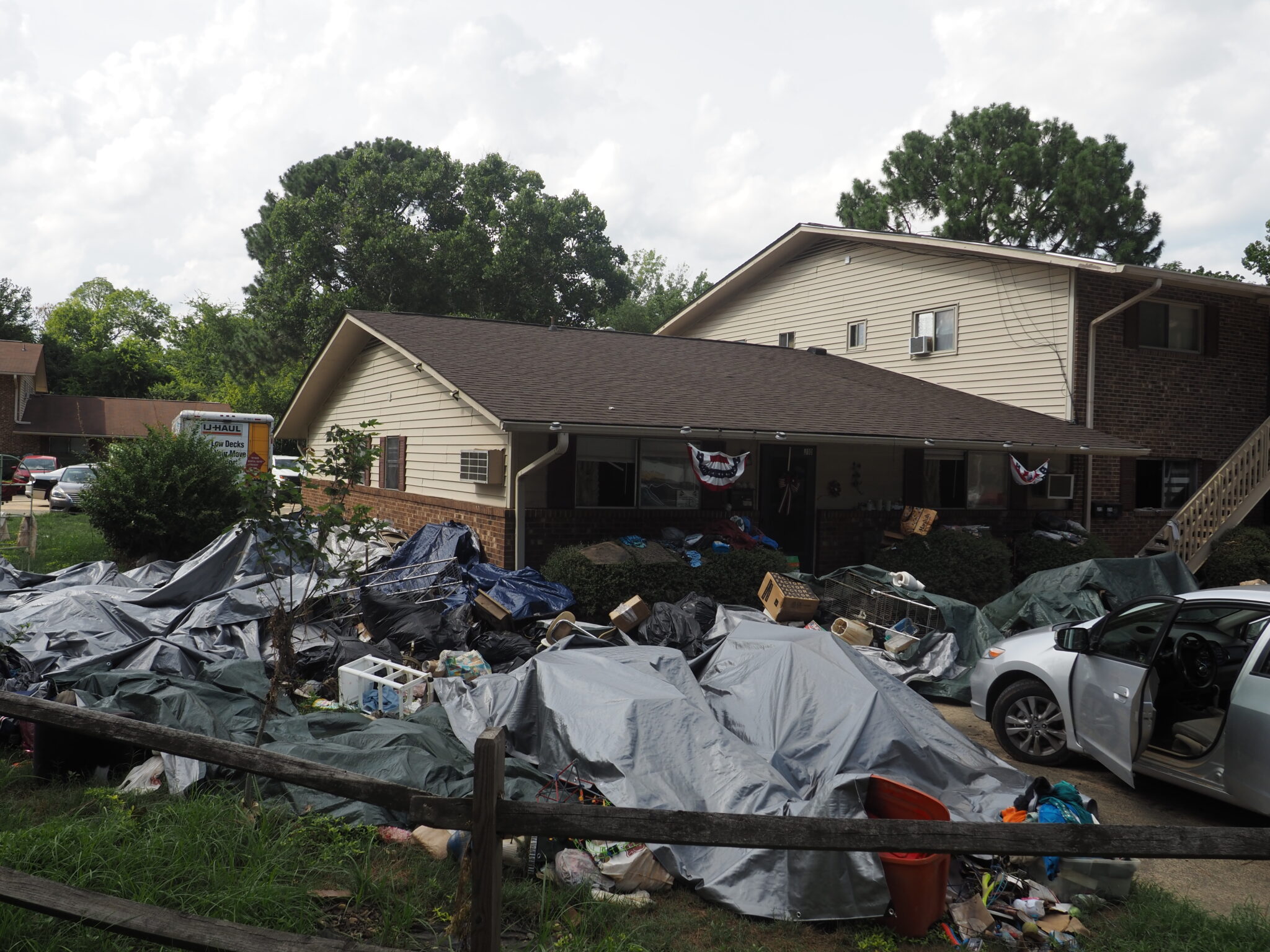 After Chantal flooding, Governor Stein surveys damage in Chapel Hill, urges federal relief A home with a yard filled with debris, much of it flood-ruined furniture covered by tarps.
