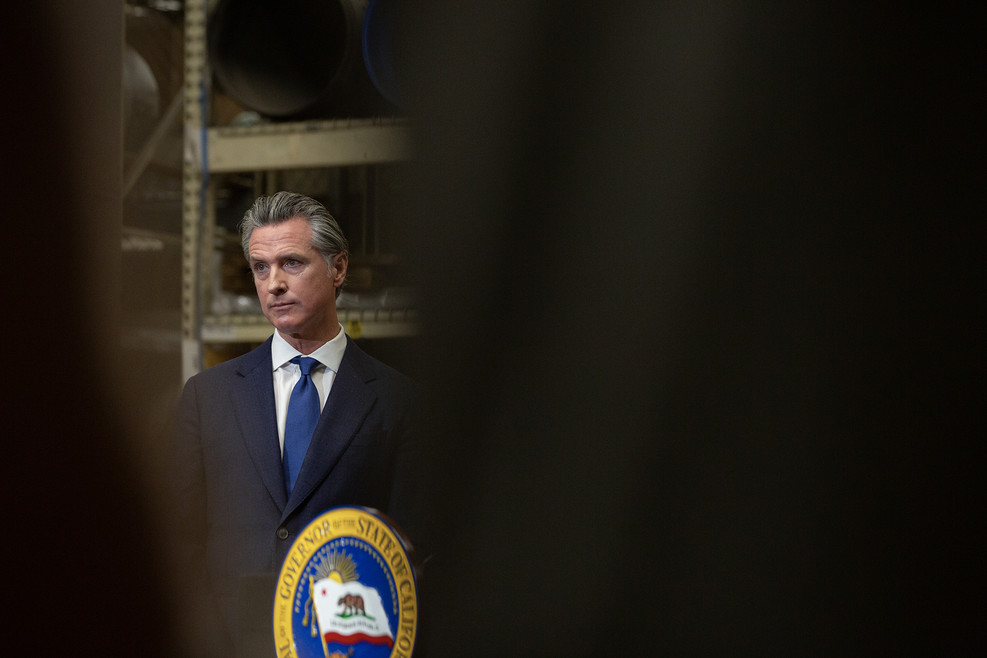 What to do about slow CA election results Viewed through a narrow, black sliver, Gov. Gavin Newsom stands at a podium while at a press conference.