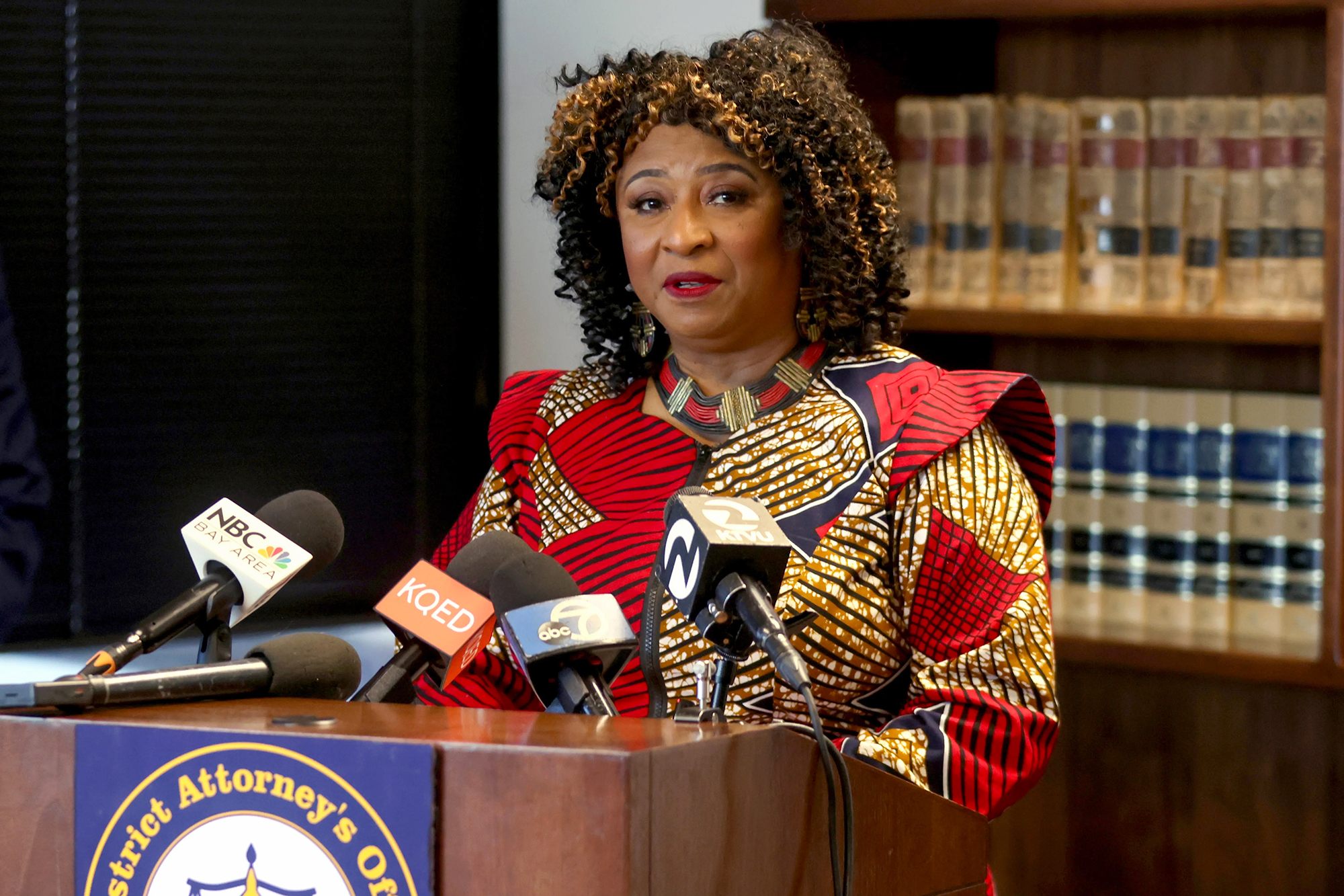 Two California prosecutors promised a different kind of justice. Voters turned on them A person wearing a red and gold pattern dress stands behind a lectern with microphones from local media outlets during a press conference. A bookshelf with law books can be seen behind them.