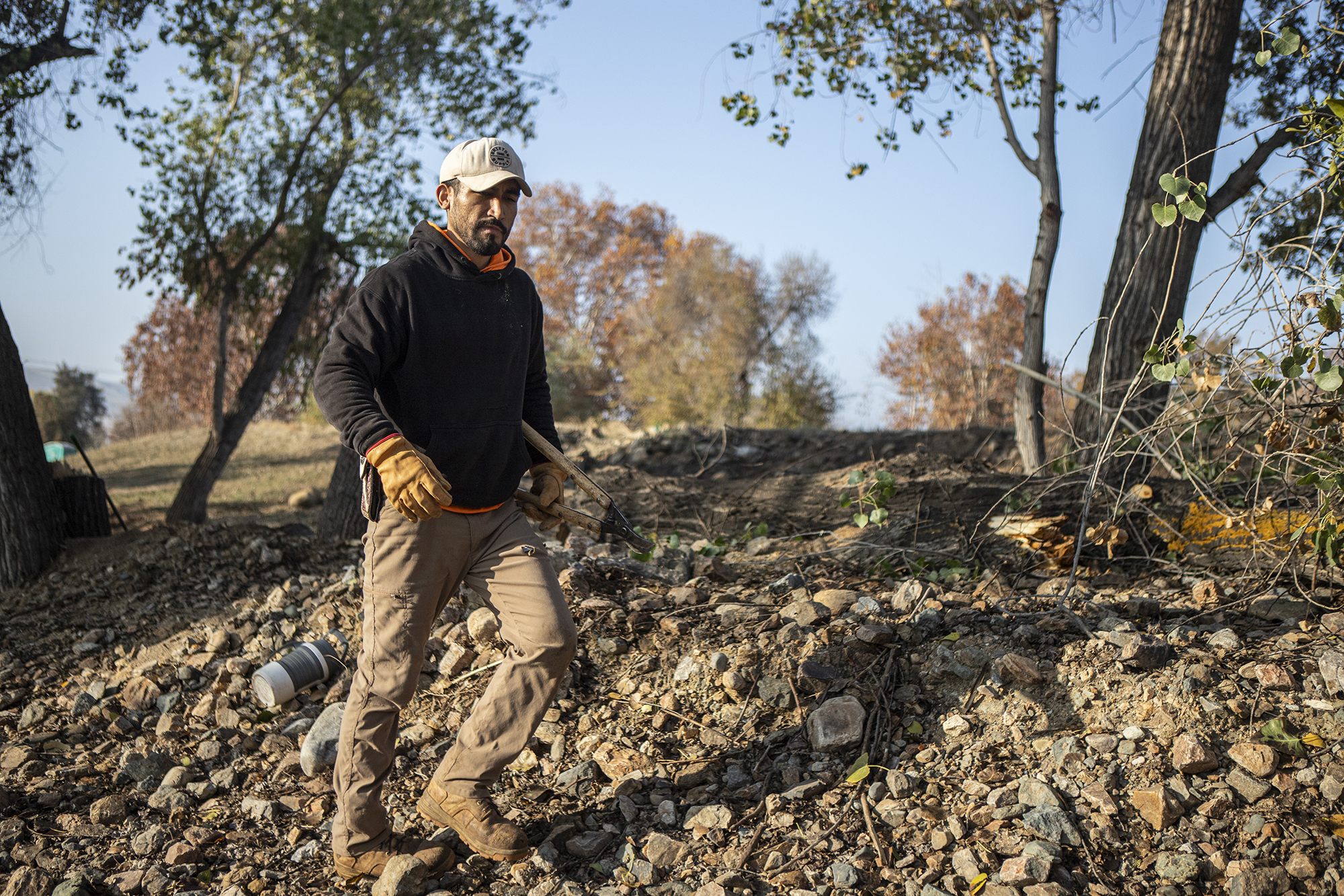 California got millions to train workers in disaster relief, but it’s leaving money on table A person in a working sweatshirt and protective work attire walks through rough terrain in a park with pruning shears under their arm.