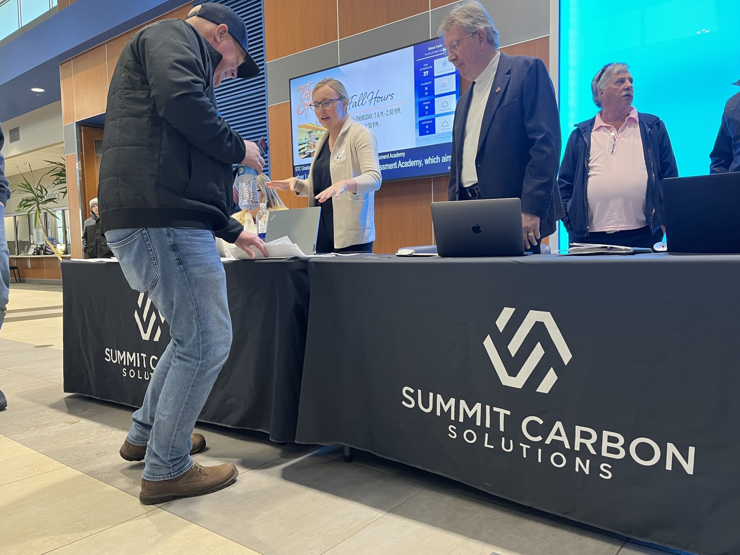 Hundreds crowd public hearing on second attempt at a carbon pipeline permit Representatives with Summit Carbon Solutions hand out information and answer questions ahead of the Public Utilities Commission public hearing in Sioux Falls on Jan. 15, 2025. (Makenzie Huber/South Dakota Searchlight)