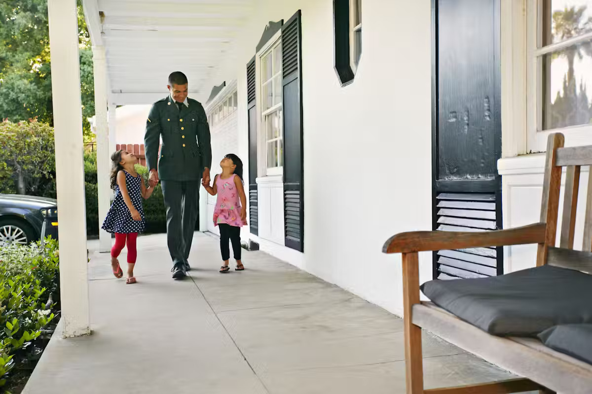 Veterans are disproportionately affected by suicide. Targeted prevention can help stem the tide.. A soldier walks along a porch holding the hands of two girls, his daughters.