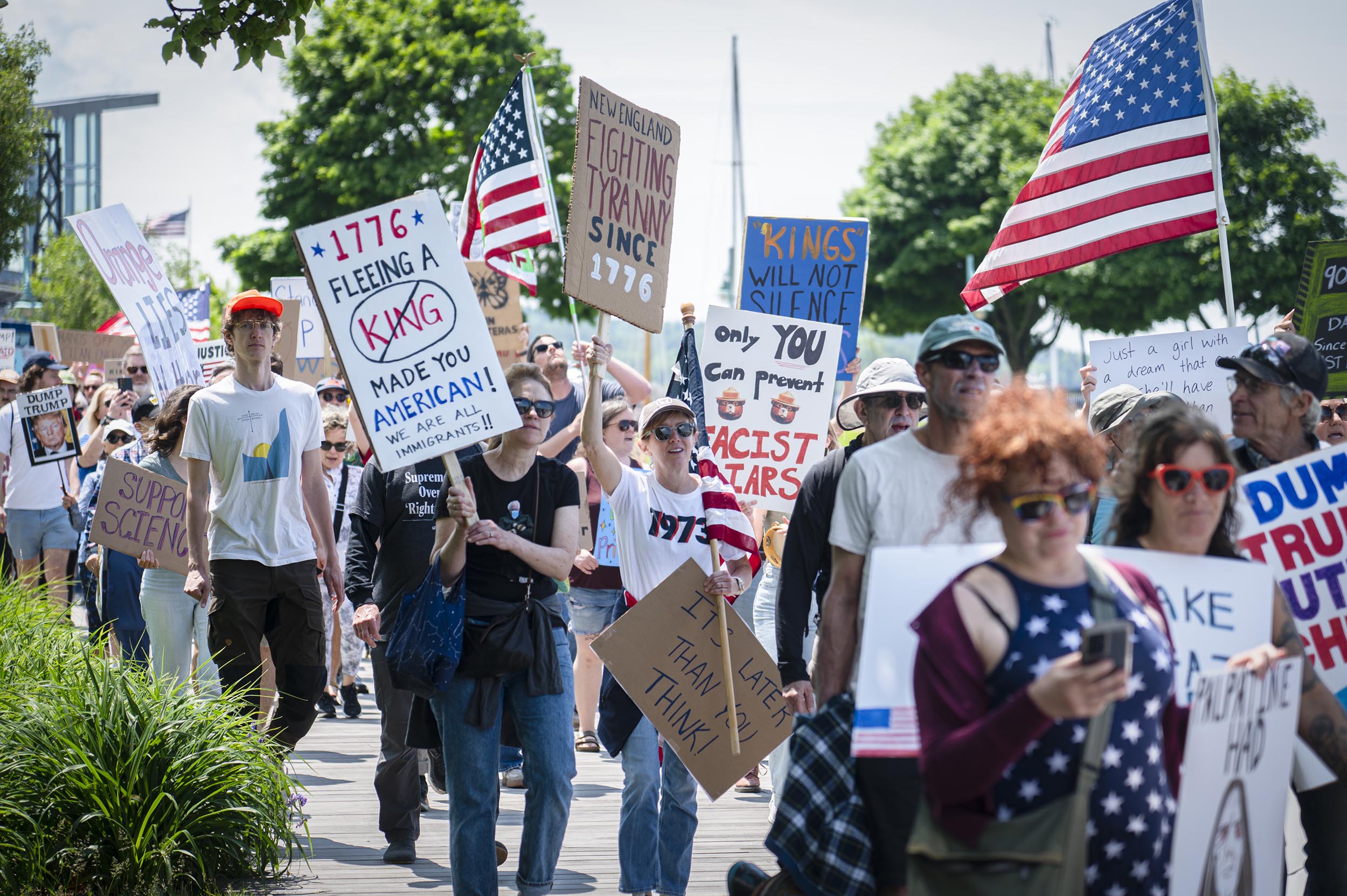 ‘No Kings Day’ draws more than 16,000 to Burlington to protest Trump and authoritarianism A group of people march outdoors holding protest signs and American flags during a daytime rally.