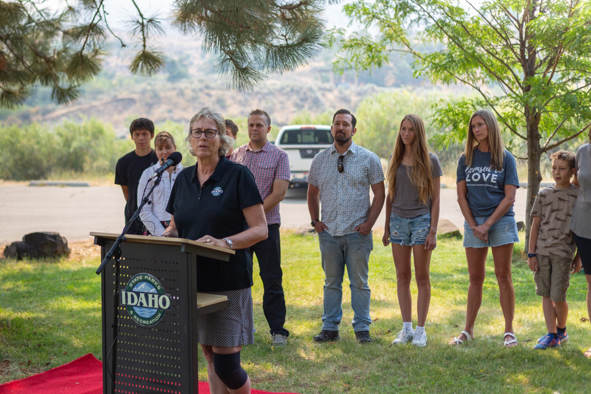 Idaho foster families to get state parks passes, outdoor trainings in public-private program Idaho Department of Parks and Recreation Director Susan Buxton speaks at a podium, in front of a line of foster parents and families.