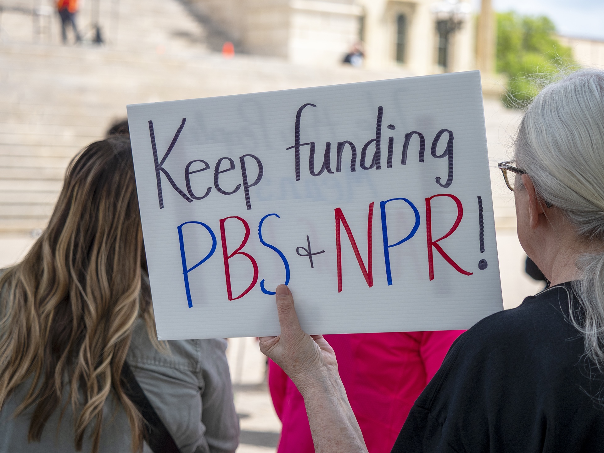 Ohio’s public media landscape at risk under potential cuts to Corporation for Public Broadcasting A protester holds a sign in support of funding for public media during a May 1, 2025, rally at the Kansas Statehouse in Topeka as part of a 50501 national day of action. (Photo by Sherman Smith/Kansas Reflector)