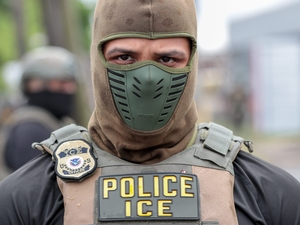 On June 10, 2026, President Donald Trump signed into law a bill providing $70 billion for immigration enforcement and detention activites over the next three years. In this photo, a U.S. Immigration and Customs Enforcement agent watches a crowd of protesters at Delaney Hall in Newark, N.J., on May 25, 2026. (Photo by Ben Ackman/New Jersey Monitor)