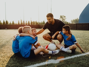 Youth sports coach with children on soccer field huddling before the final tournament match - stock photo