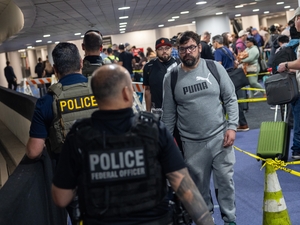 A traveler looks at Immigration and Customs Enforcement (I.C.E.) agents as they walk around the end of the line at Terminal E at George Bush Intercontinental Airport on March 24, 2026 in Houston, Texas. The travel disruptions continue as hundreds of TSA agents quit or work without pay during a partial government shutdown. U.S. President Donald Trump said ICE agents will be deployed to U.S. airports on Monday, with border czar Tom Homan in charge of the effort. (Photo by Antranik Tavitian/Getty Images)