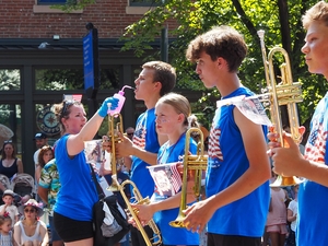 A chaperone from Nebraska squirted water into the mouth of a Grand Island Senior High School marching band member at the Capitol Hill Fourth of July Parade on Saturday, July 4, 2026 in Washington, D.C. The band marched in the smaller parade after the National Independence Day Parade was canceled due to the extreme heat. (Photo by Ashley Murray/States Newsroom)