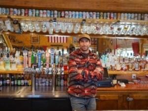 Rock Shop owner Anthony Prate behind the bar that he renovated and reopened to the public. Among the artifacts and curiosities Prate has decorated the space with is his uncle’s collection of old beer cans, which includes several rare brands. (Katie Klingsporn/WyoFile)