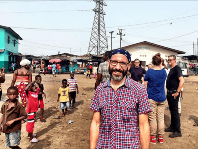 shows a man in a kerchief standing in an African marketplace, smiling at the camera