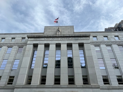 The courthouse is shown at a looming angle with clouds swirling above. It is a pale-colored building with columns and the words
