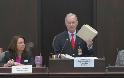 Rep. Frank Iler holds up a file folder as he speaks into a microphone at the legislature