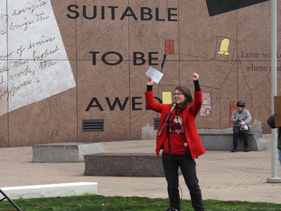 Nyssa Tucker stands in Halifax Mall, arms raised, speaking into a microphone.