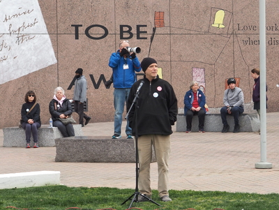 Wearing a beanie and jacket, Mark Peifer speaks at a microphone in Halifax Mall.