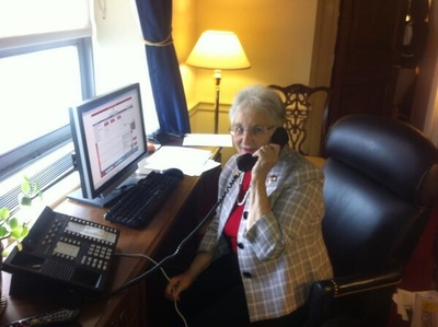 Virginia Foxx speaks into a landline telephone sitting at a desk in her congressional office.
