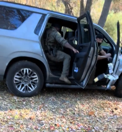 A truck of armed agents drives away as one throws a wallet out the door.