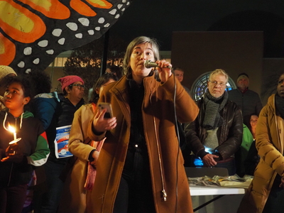 A woman speaks into a microphone in front of a large butterfly sign.