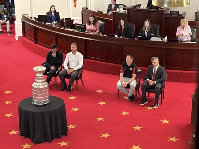 Four men sit in chairs on the floor of the NC Senate beside the Stanley Cup.