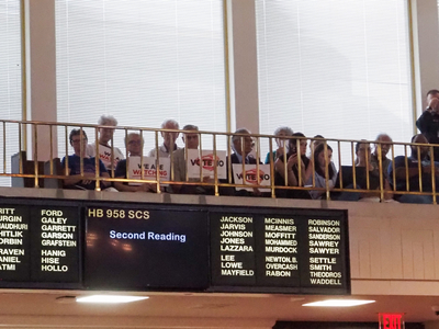 Critics of a NC election sit in the Senate gallery with Vote No signs on July 28, 2026. (Photo: Claire Michal/NC Newsline)
