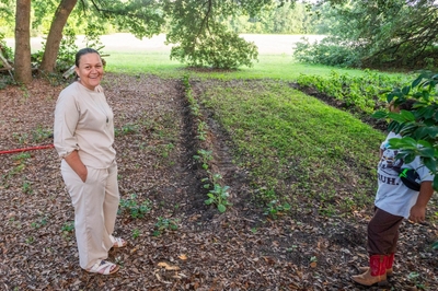 Angie Lowery stands next to rows of plants growing in rows in her backyard garden.