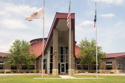A photo of a large government building. In front of it are three flagpoles: on the left is the Lumbee Tribe flag; the American flag is in the center; the North Carolina flag is on the right.