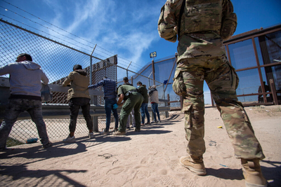 A Texas National Guardsman observes as Border Patrol agents pat down migrants who have surrendered themselves for processing, May 10, 2023. (Photo by Corrie Boudreaux for Source NM)