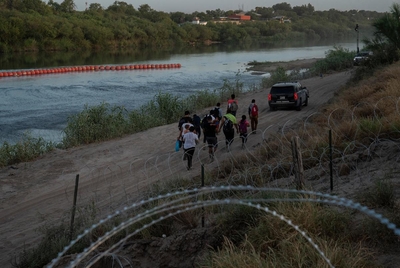 A group of migrants follow a state trooper vehicle after turning themselves in in Eagle Pass, Texas on July 29, 2023. They crossed through a cap in the concertina wire in the Urbina’s property. Some will be sent back after being arrested for trespassing private property without allowing them to go through the immigration process in the U.S.