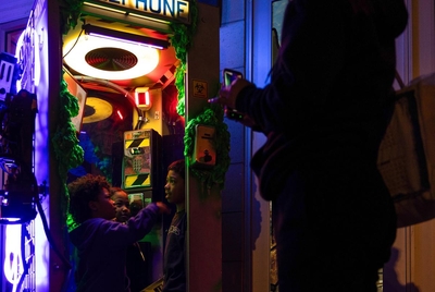 Children listen to clues on a telephone booth landline as part of an interactive installation on the square on {was} in Denton, Texas. There are three telephone booths located around town that people are encouraged to seek out and solve clues.