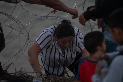 A Colombian mother goes through concertina wire to turn herself in with her daughter and other people in Eagle Pass, Texas on July 29, 2023. As there is concertina wire installed along the Urbina’s property, migrants are told to walk to the end of the property, taking them approximately an hour from that point. Many make that walk which can be difficult to do through slippery rocks in the water, the current and the inclined river bank, while some find spots through the concertina wire and manage to get th