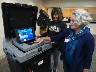 Two women stand near an election tabulator machine