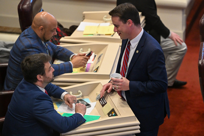 A man in a suit talking to another man in a suit sitting in a desk.
