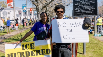 Two people holding signs saying "Ice Murdered" and "No war for oil"