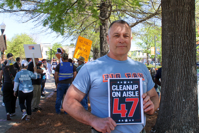 A man holding a sign at the Auburn No Kings protest.