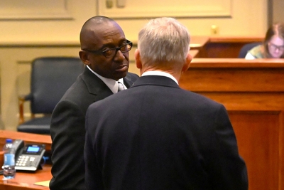 A man in a suit and glasses listening to another man