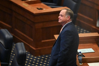 A man in a blue suit leaning against a desk