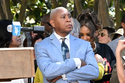 A man in a blue suit and blue patterned tie with his arms folded