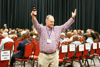 A man in a checkered shirt holding up a beer
