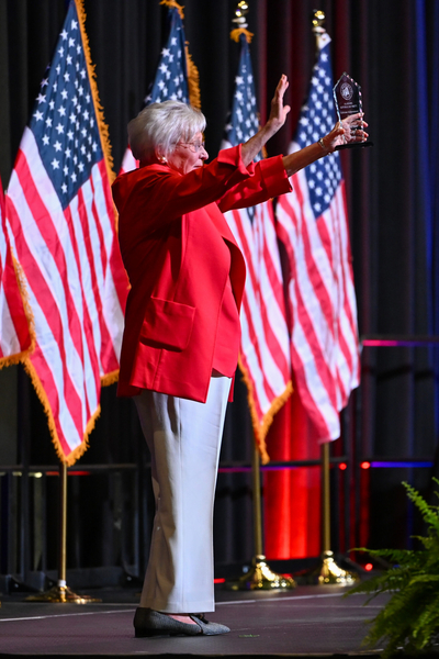 A woman in a red suit with her hands raised.
