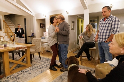 Several family members surround Valentine, who is seated, as her parents dance in the middle of a room.