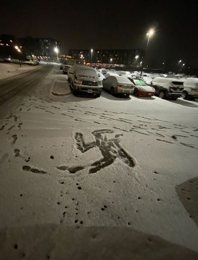 A snow-covered parking lot with footsteps and a swastika drawn in it.