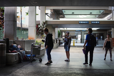 Michael Warden, from left, sleeps at the Daniel K. Inoyue International Airport terminal 2 departure area as IHS’ Sarah Rodrigues, Jo, Tiare Akana and executive director Connie Mitchell work their way through the airport during the Point In Time homeless count Monday, Jan. 26, 2026, in Honolulu. (Kevin Fujii/Civil Beat/2026)