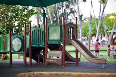 A playground sits empty in the shade as a family hangs out in the background