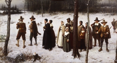 Around a dozen people walk through a clearing in the woods, with snow on the ground.