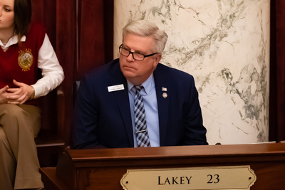 Idaho Sen. Todd Lakey sits at his desk in the Senate chambers. He wears a nametag and a dark blue suit