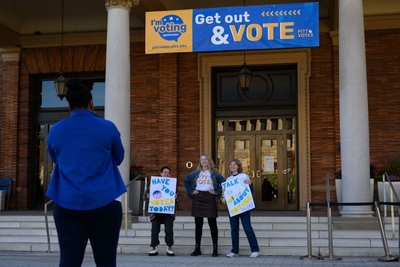 Three young women hold signs about voting while standing outside.